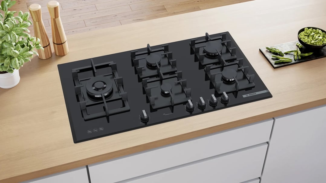 Black Bosch gas cooktop with five burners on a light wooden countertop