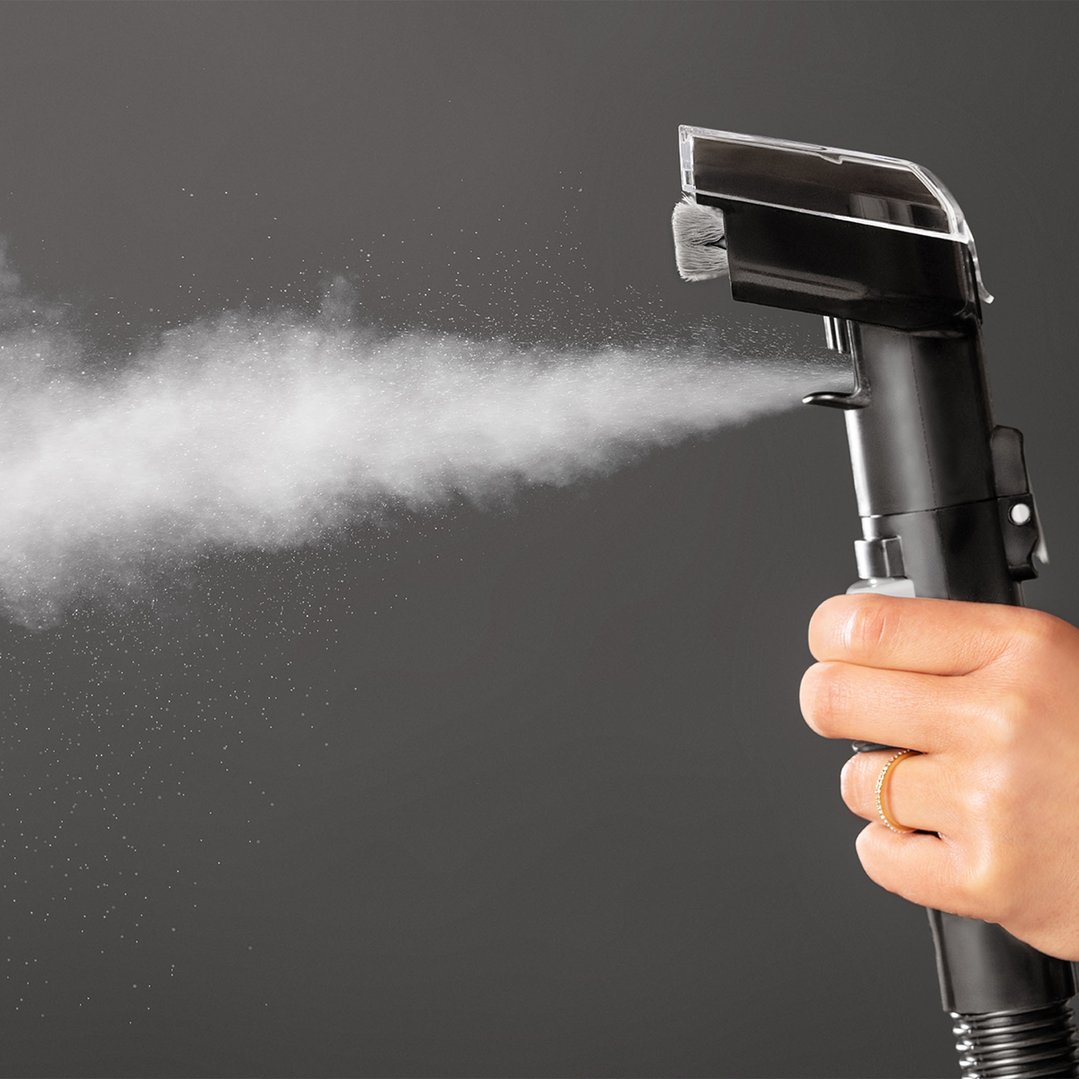 Hand holding a BISSELL SpotClean HydroSteam vacuum cleaner emitting steam