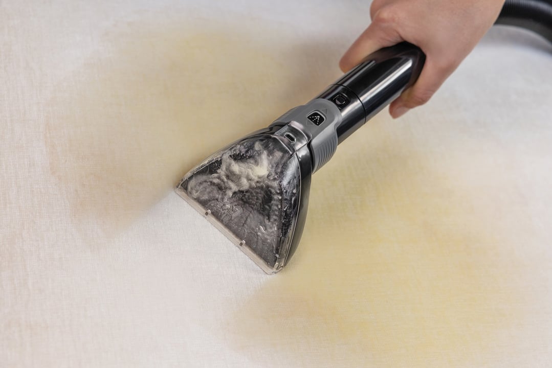 Hand using a carpet and upholstery cleaner to clean a light-colored carpet