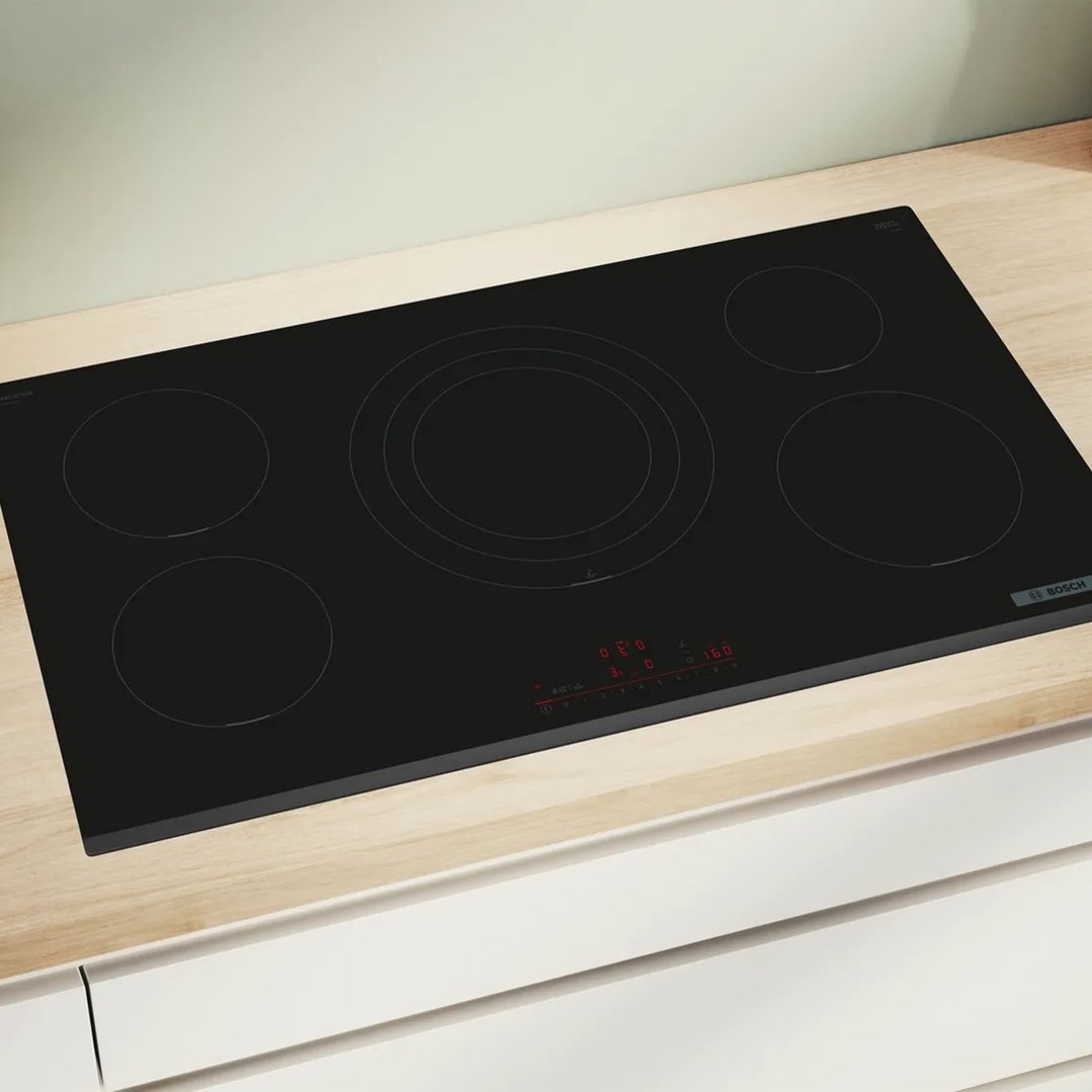 Black induction cooktop with five cooking zones built into a light wood countertop