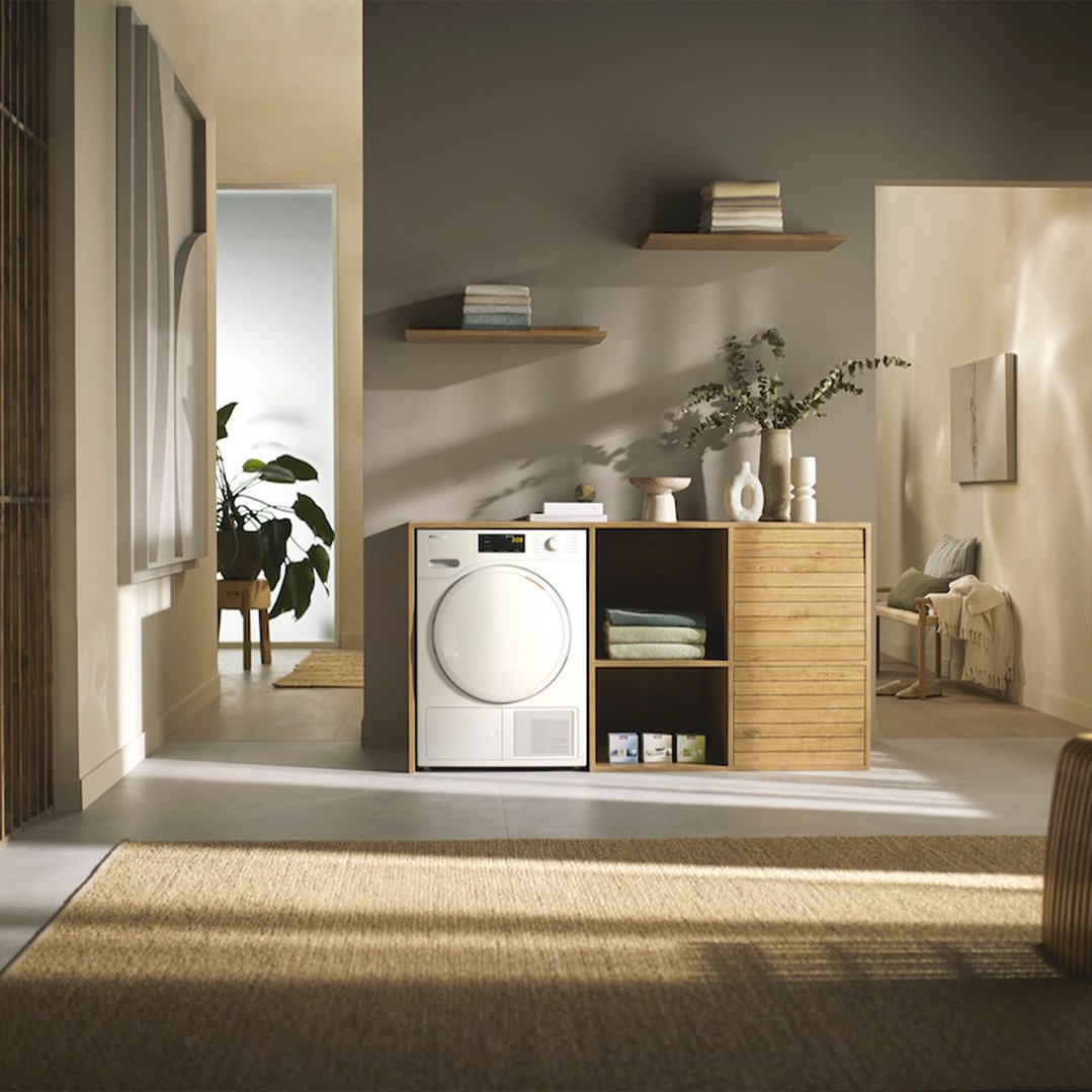White heat pump dryer integrated into a wooden cabinet in a modern room