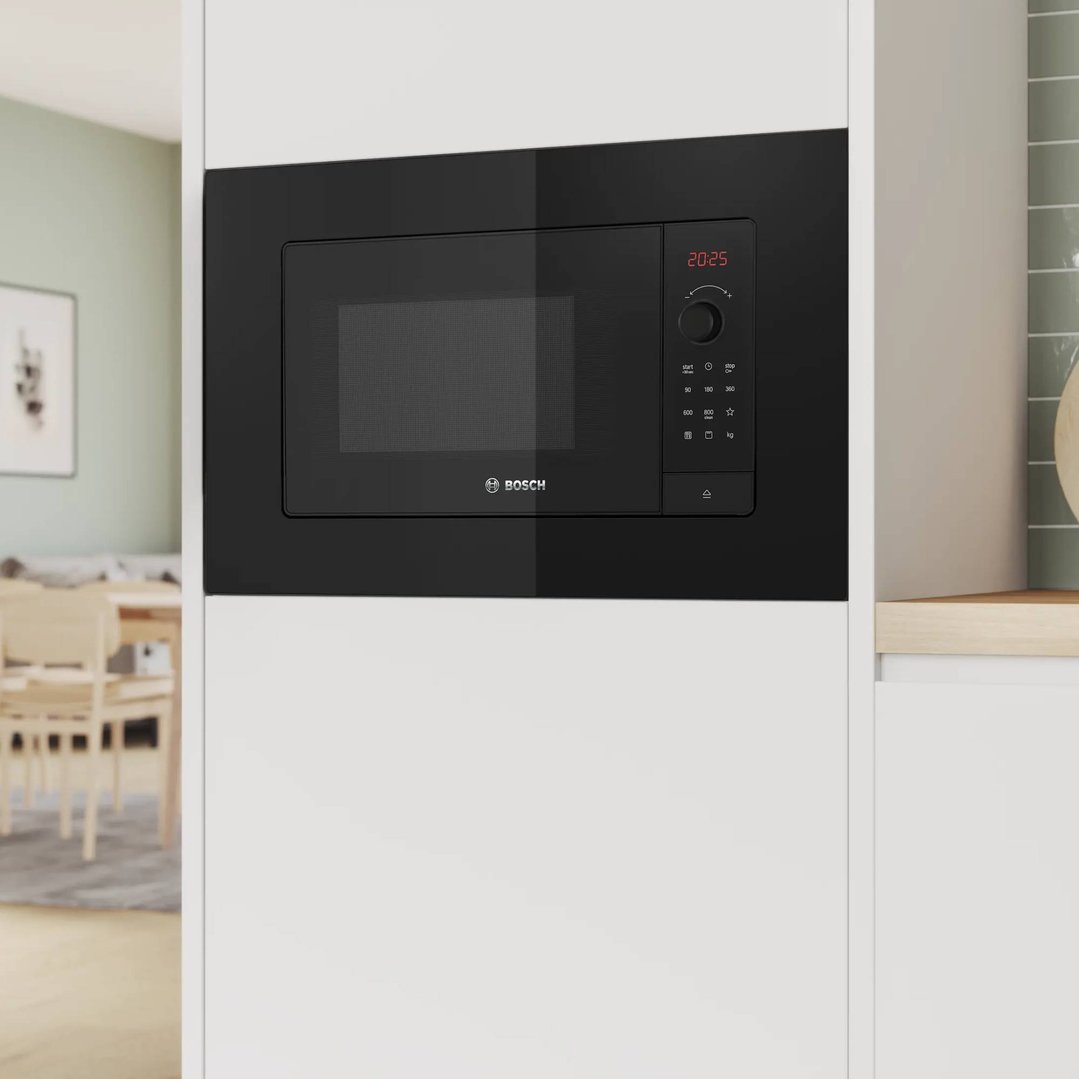 Built-in black microwave oven in a white kitchen cabinet with a dining area