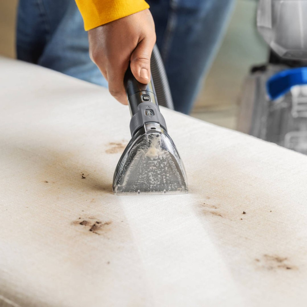 Hand using a carpet and upholstery cleaner on a dirty white surface