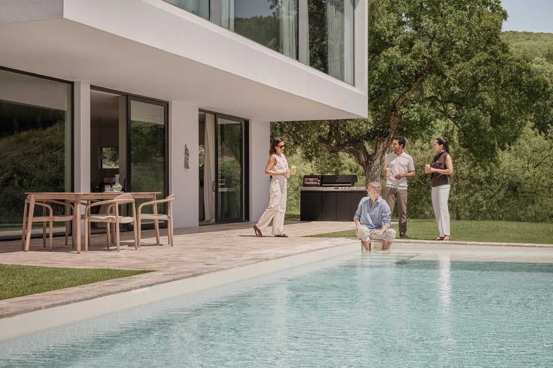 People gathered around an Essence Outdoor Kitchen BBQ by a pool