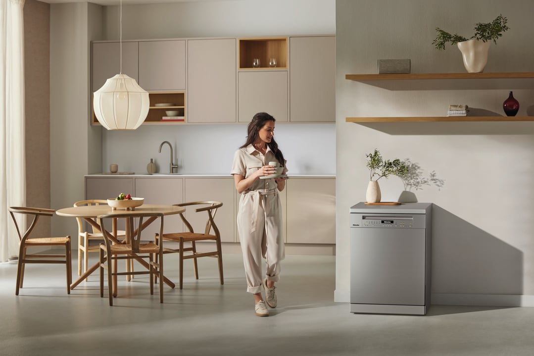 Woman holding dishes in a modern kitchen with a freestanding dishwasher