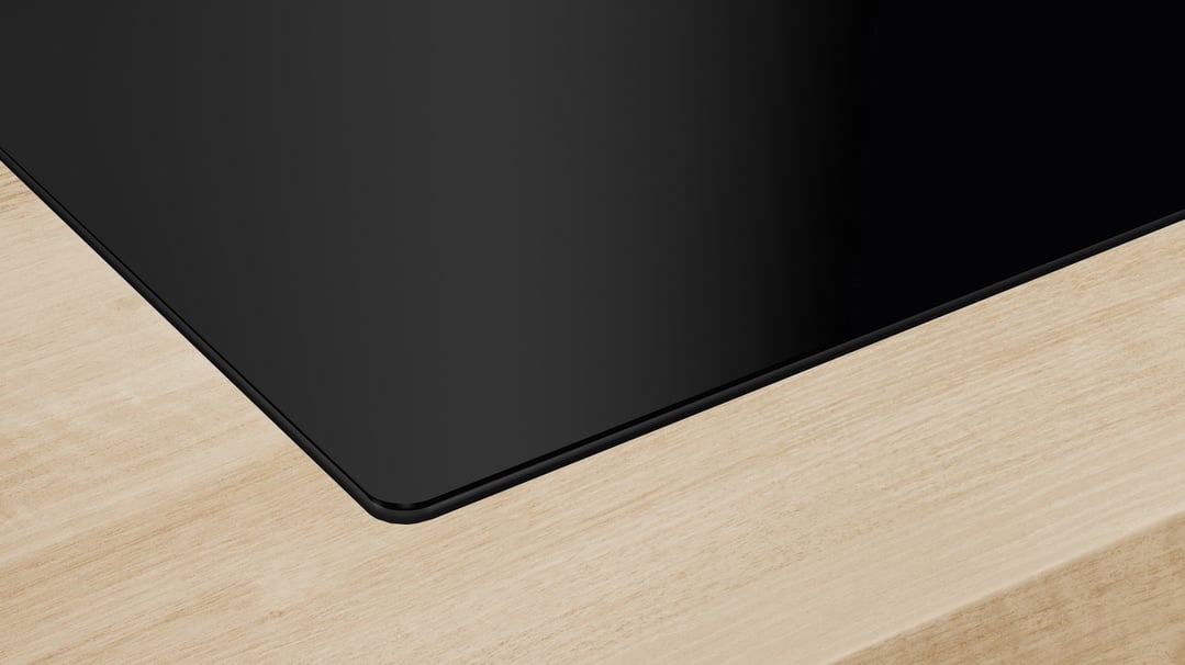 Close up of a black induction cooktop built into a light wood countertop