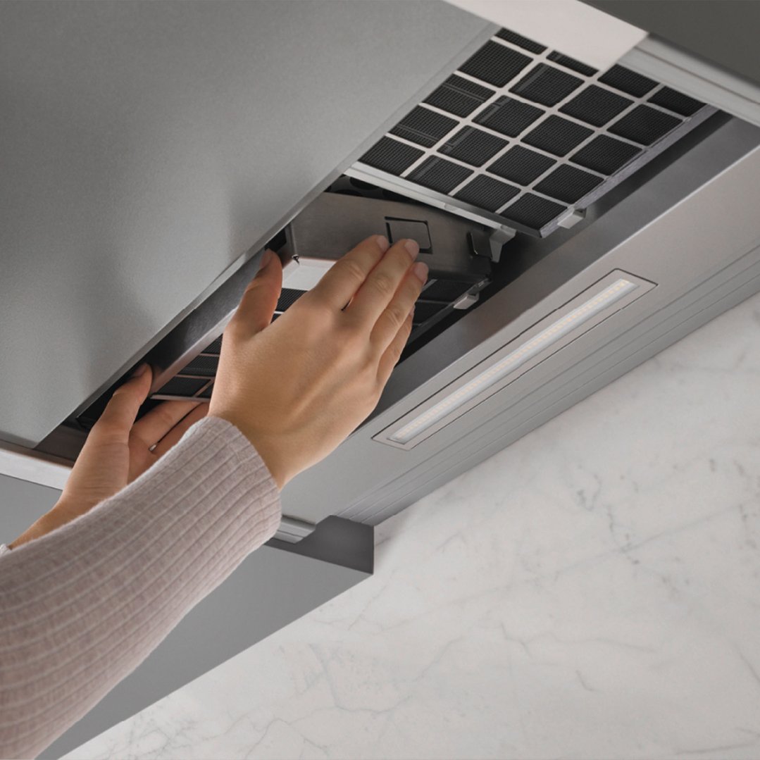 Hands removing the filter from a stainless steel rangehood with LED lighting