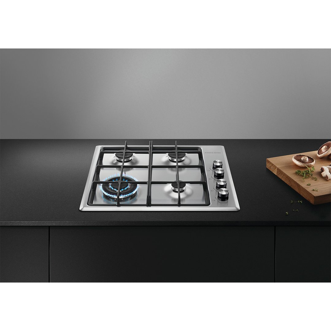 A Fisher & Paykel 4 burner gas cooktop with one burner lit, in a kitchen