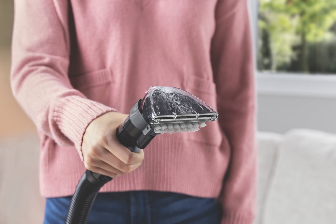 Person holding a carpet and upholstery cleaner with a brush head