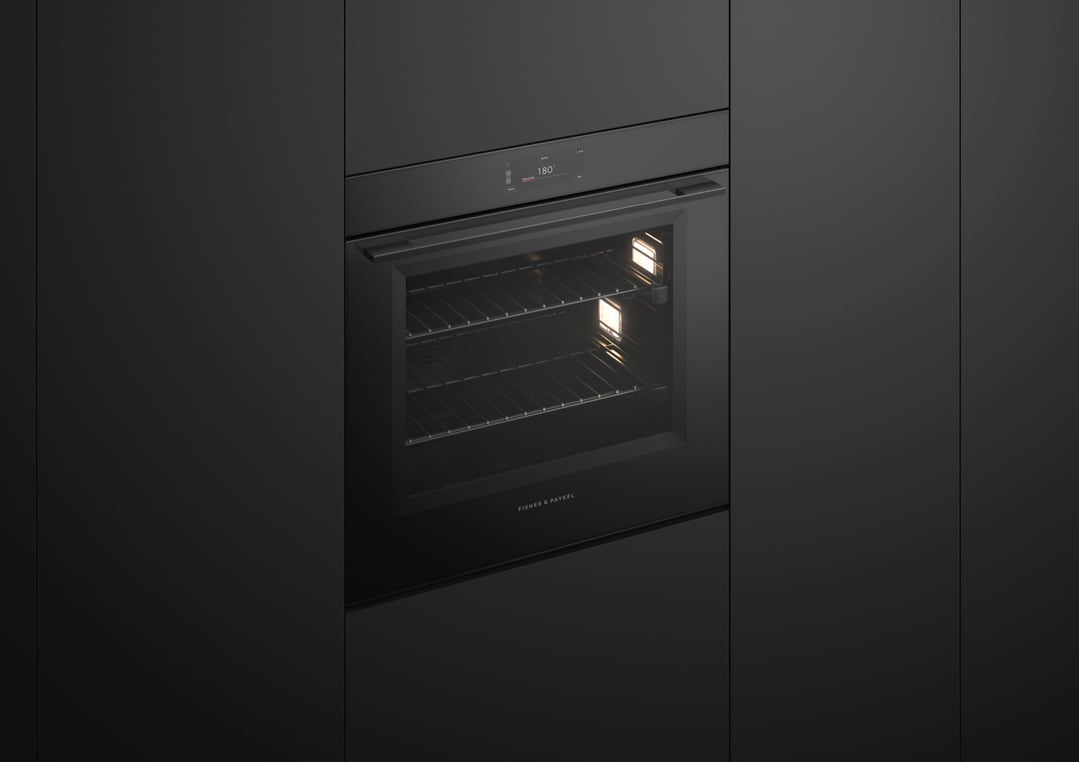 Black built-in oven with illuminated interior in a dark kitchen setting