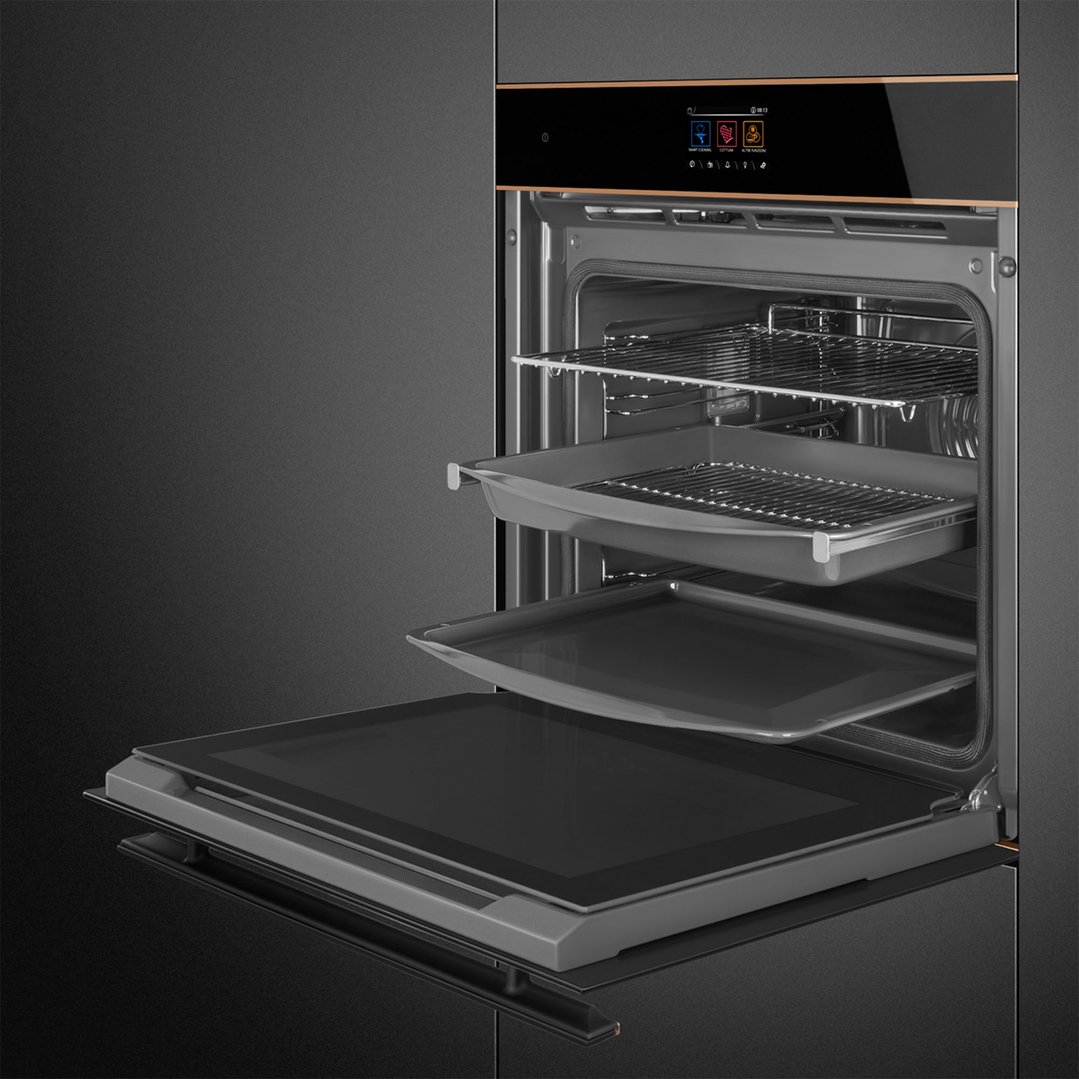 Open oven with multiple racks and trays in a dark kitchen setting