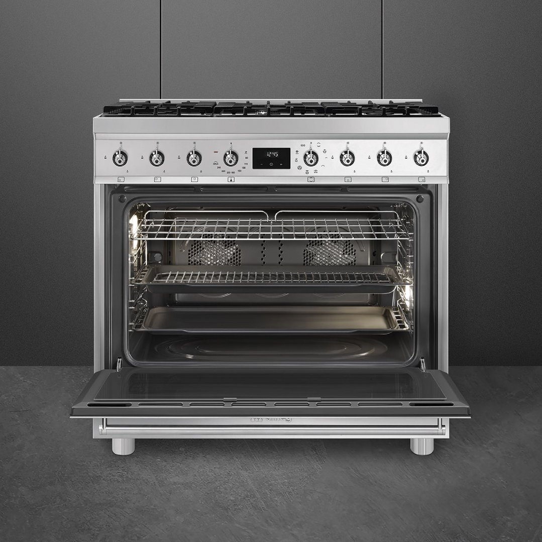 Stainless steel freestanding cooker with oven door open in a dark kitchen setting