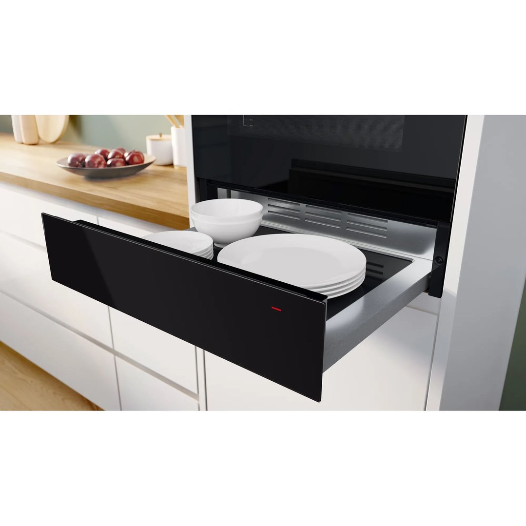 Black warming drawer open with white plates and bowls inside a modern kitchen