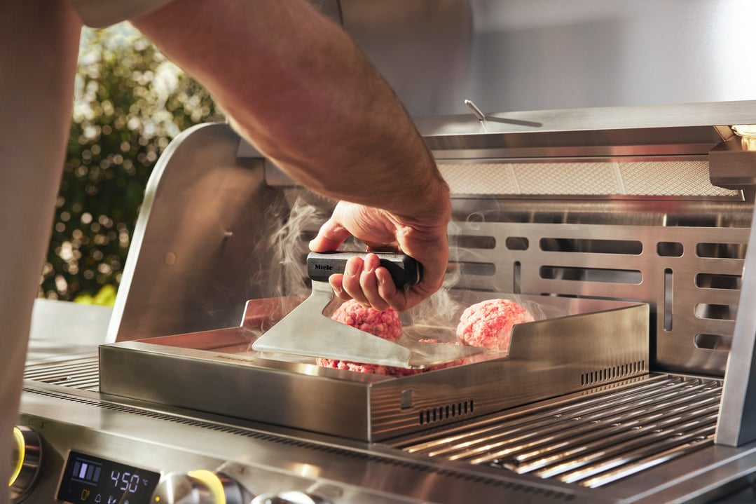 Person pressing raw burger patties on a Miele Griddle Master Outdoor BBQ Griddle Plate