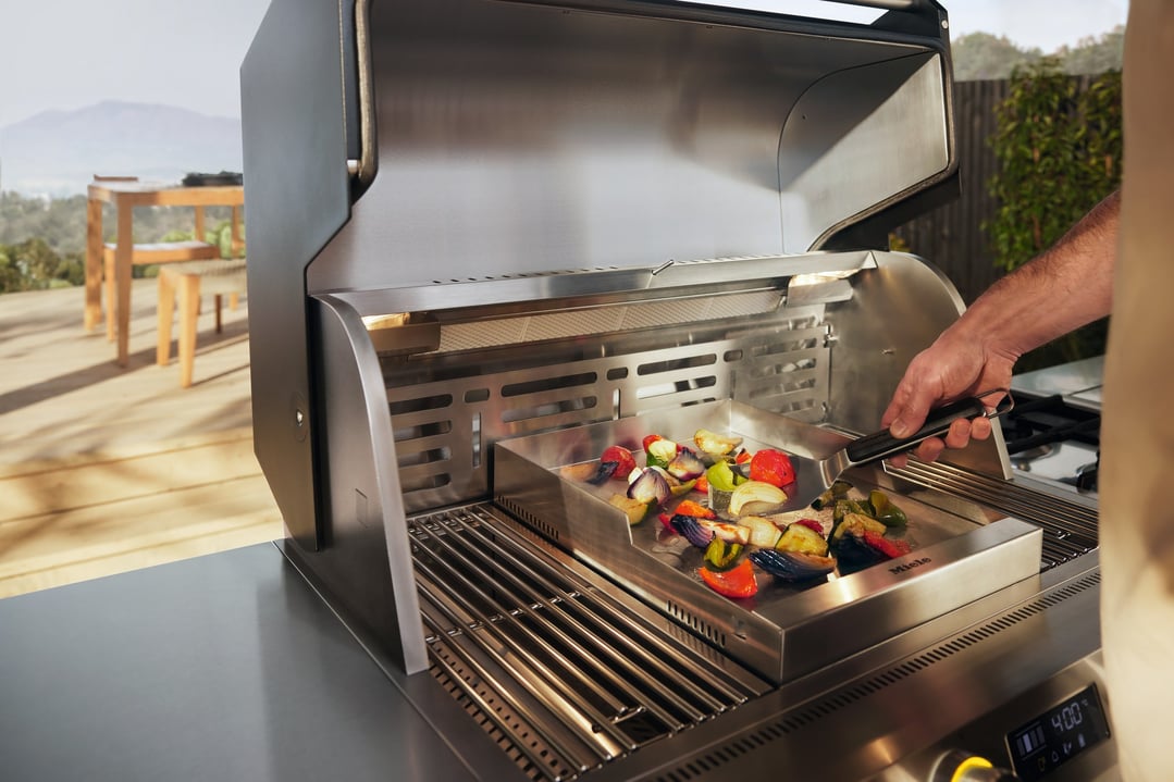 Person grilling vegetables on a Miele outdoor BBQ griddle plate