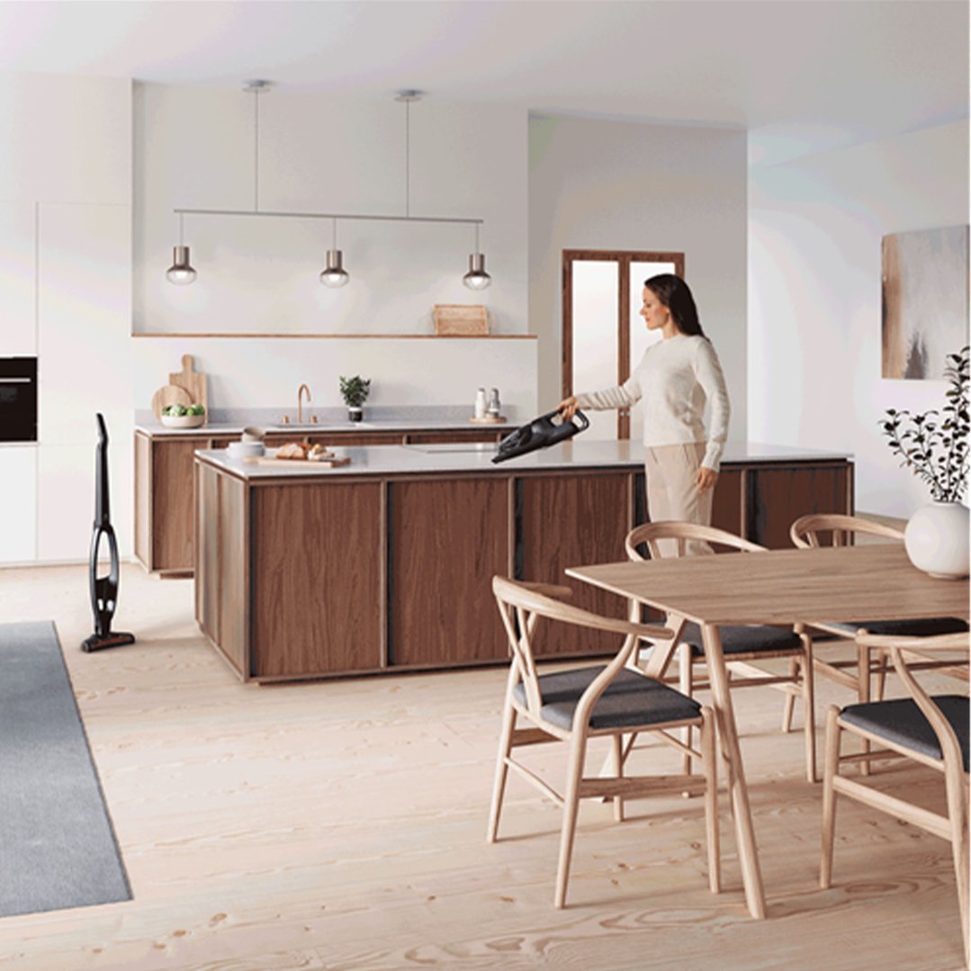 Woman using a cordless vacuum to clean a kitchen island in a modern home