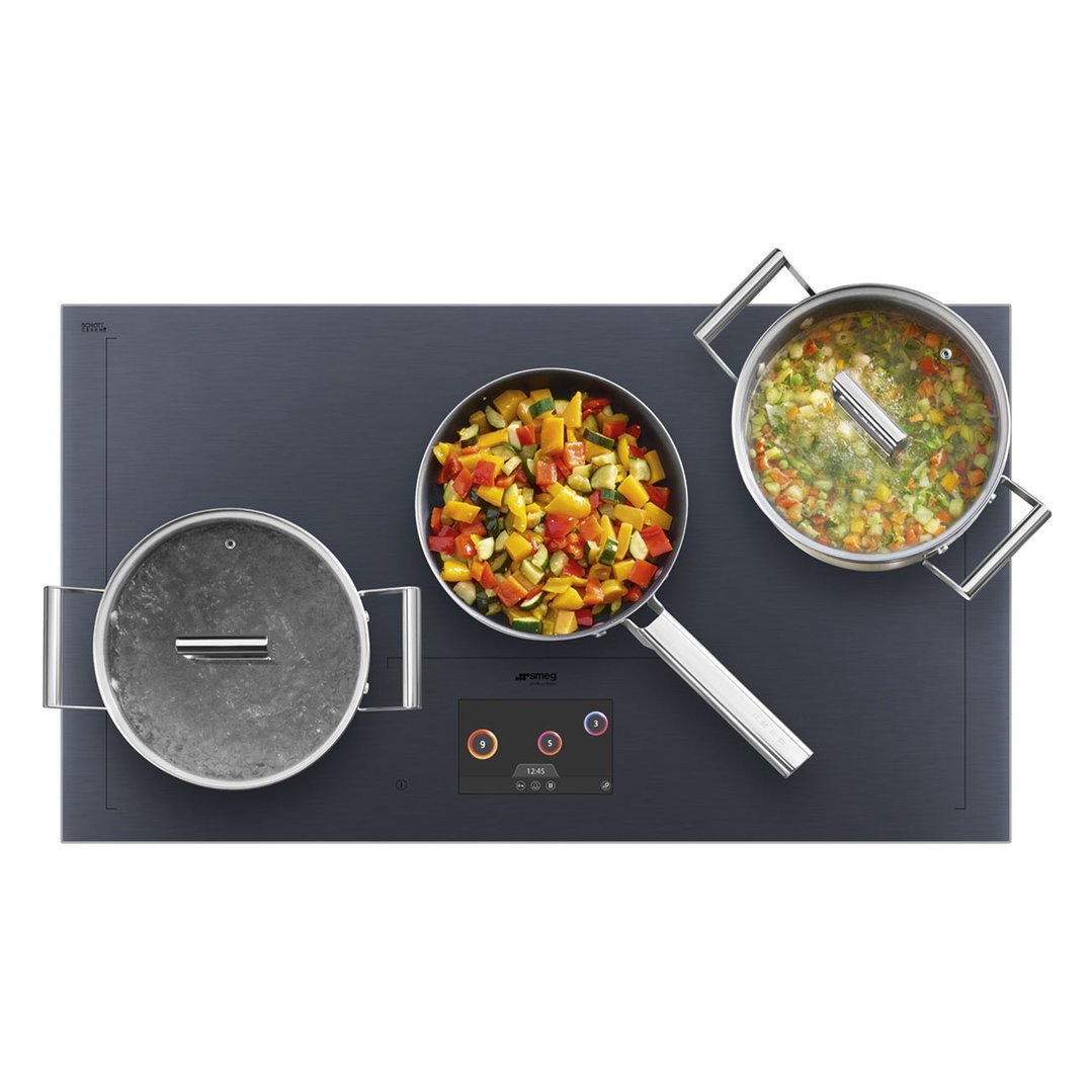 Overhead view of a Smeg induction cooktop with three pots cooking vegetables