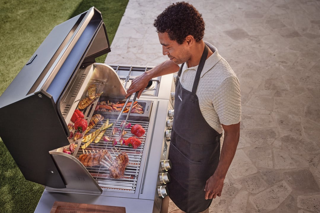 Man grilling vegetables and meat on an outdoor BBQ with the lid open