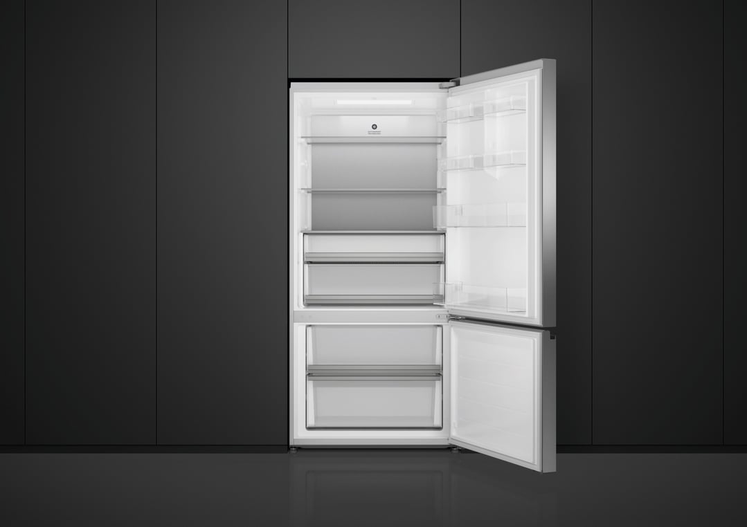 Open stainless steel bottom mount fridge in a dark kitchen setting