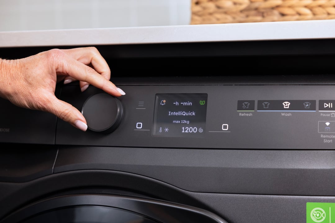 Hand adjusting settings on the control panel of a dark grey dryer