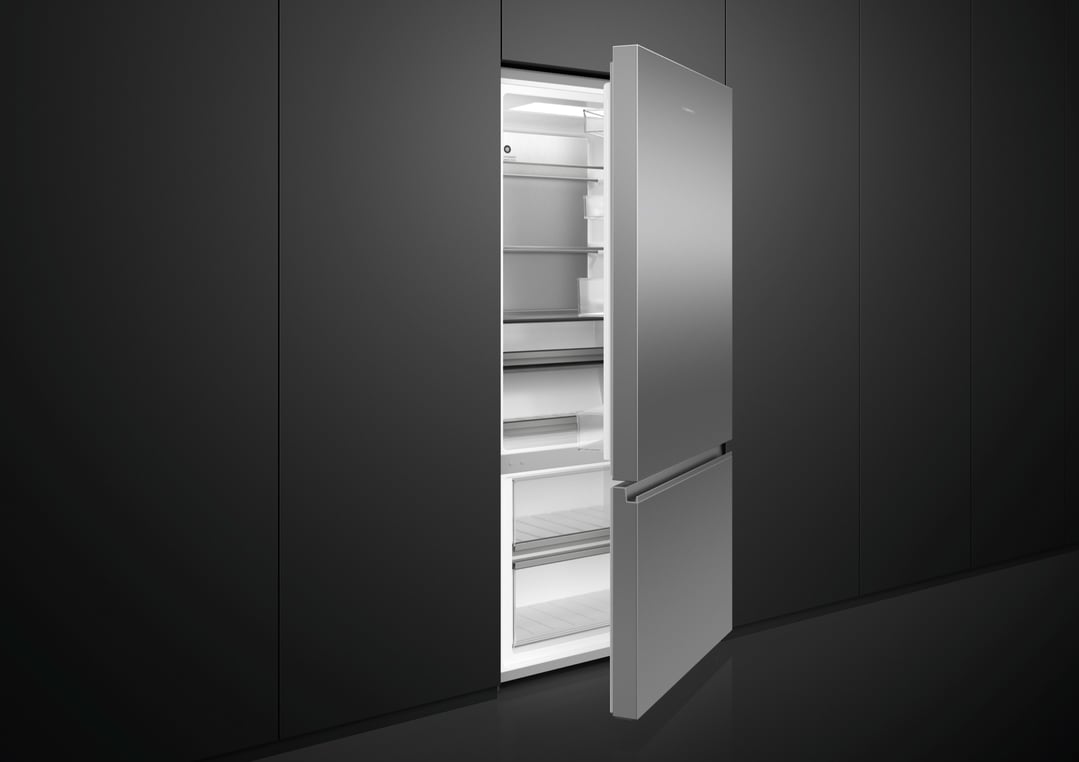 Stainless steel bottom mount fridge with doors open in a dark kitchen