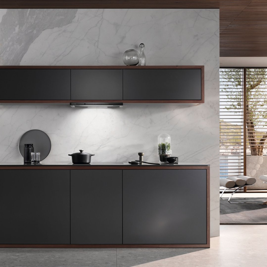 A slideout rangehood installed above a cooktop in a modern kitchen with dark cabinetry