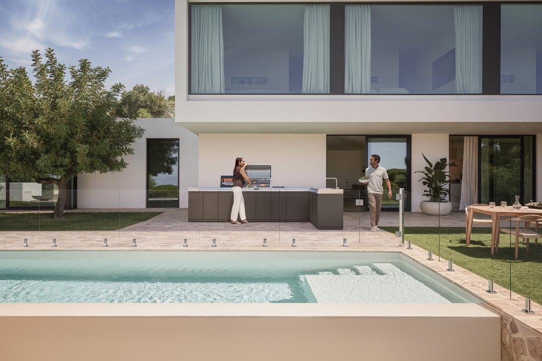 Man and woman cooking on an outdoor kitchen BBQ by a pool