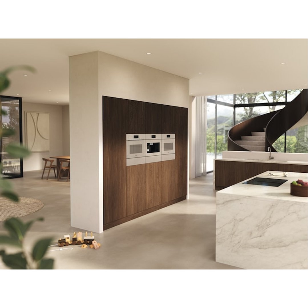 Three ovens built into a dark wood wall in a modern kitchen with a spiral staircase