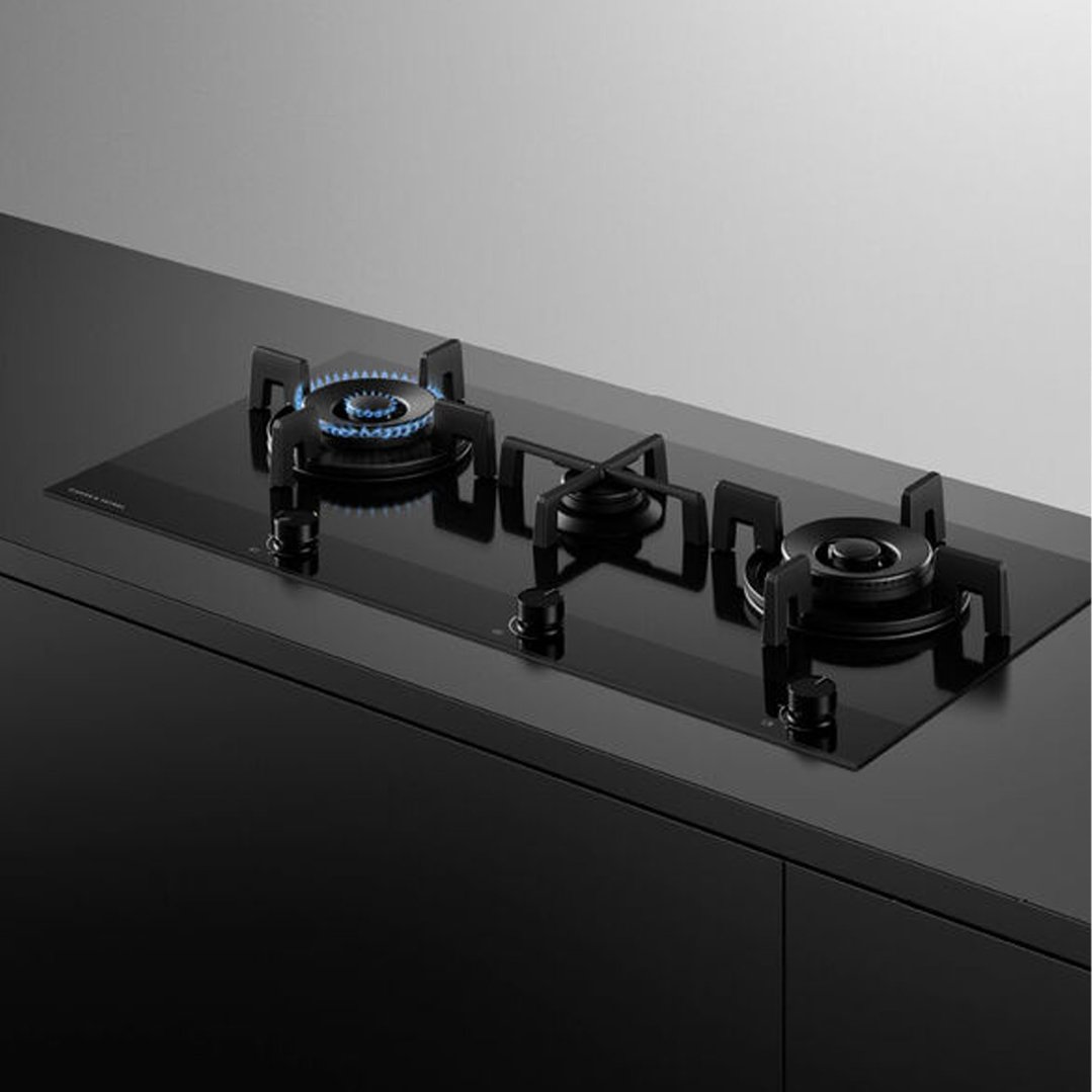 Black gas on glass cooktop with three burners, one with blue flame, in a kitchen