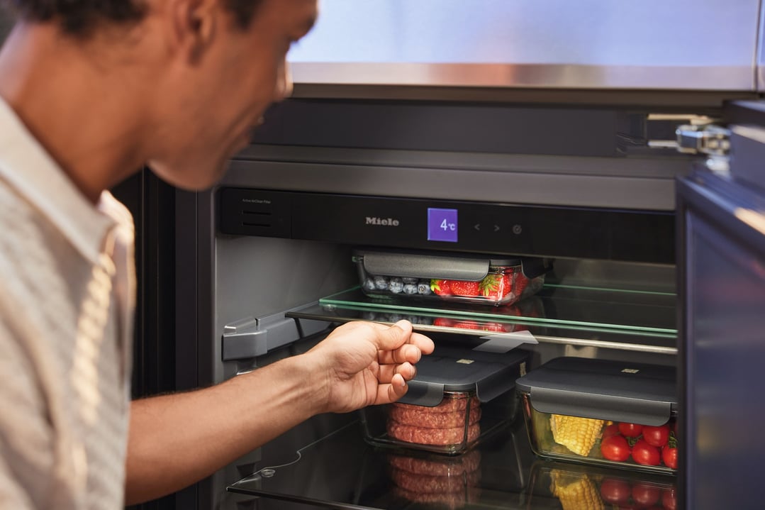 Man's hand reaching into an open outdoor fridge module filled with food containers