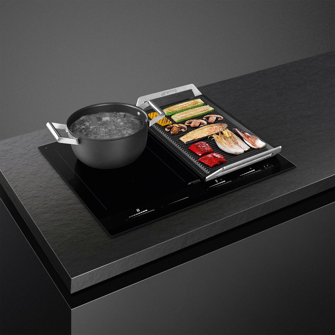 Black induction cooktop with a pot of boiling water and a grill pan with vegetables