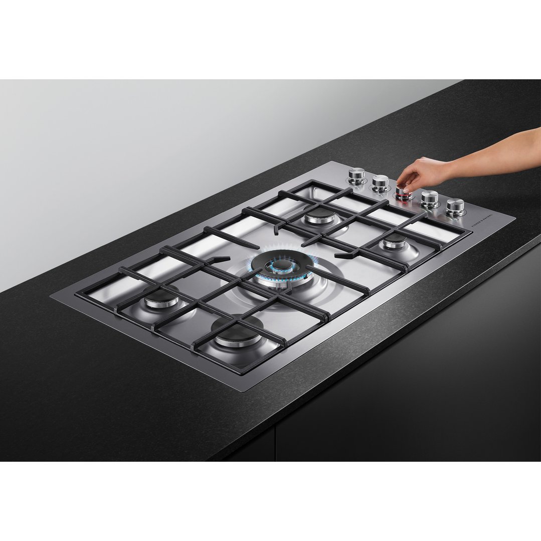 Hand adjusting the control knob of a gas cooktop with a lit burner