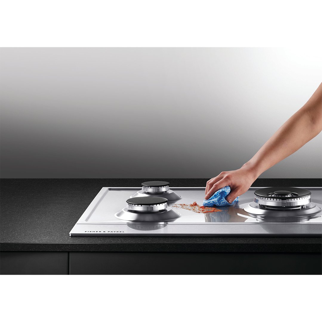 Hand wiping a Fisher & Paykel gas cooktop with a blue cloth