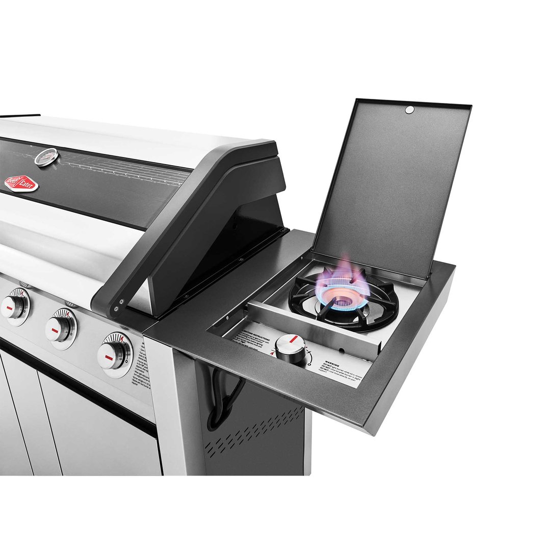 Close up of a barbeque with a lit side burner and control knobs