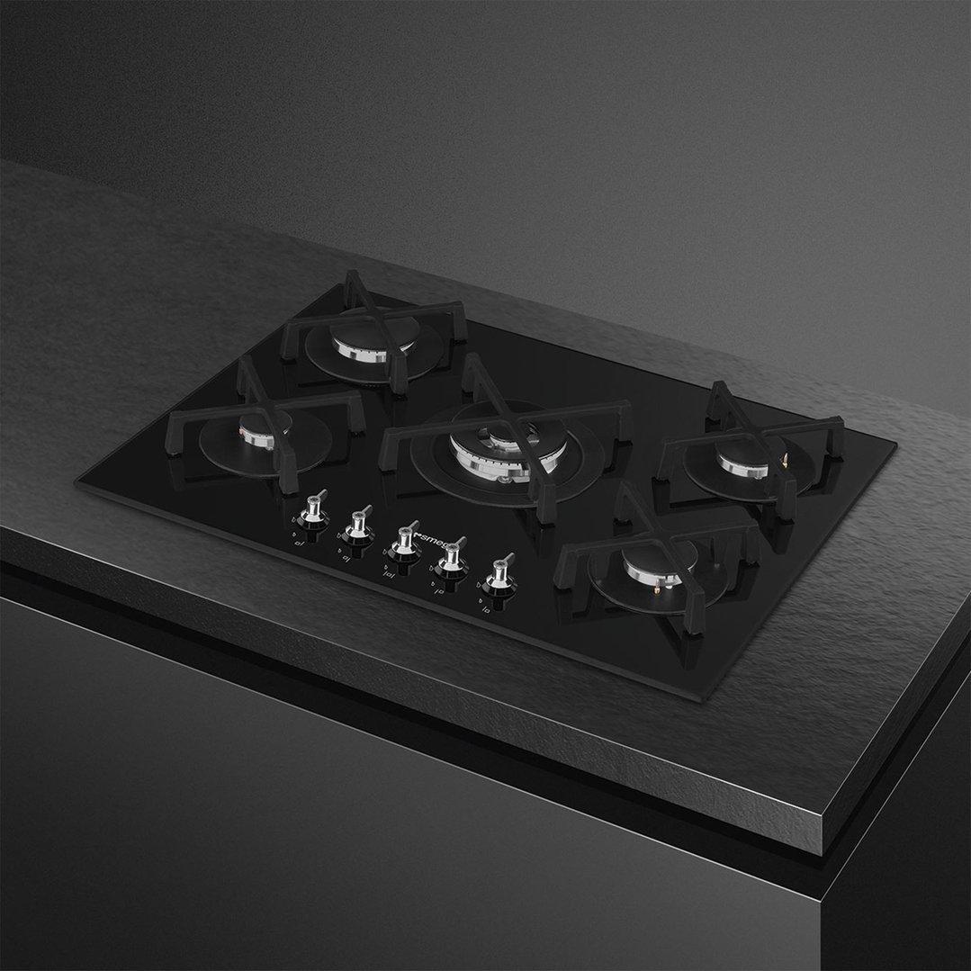 Black glass gas cooktop with five burners and controls on a dark countertop