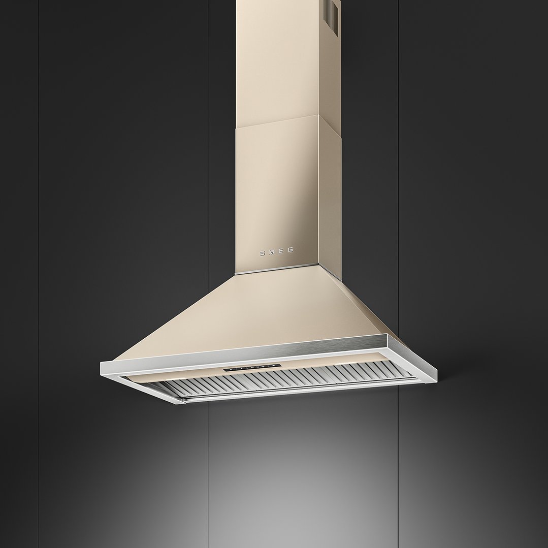 A champagne-colored Smeg rangehood hangs from the ceiling against a dark wall
