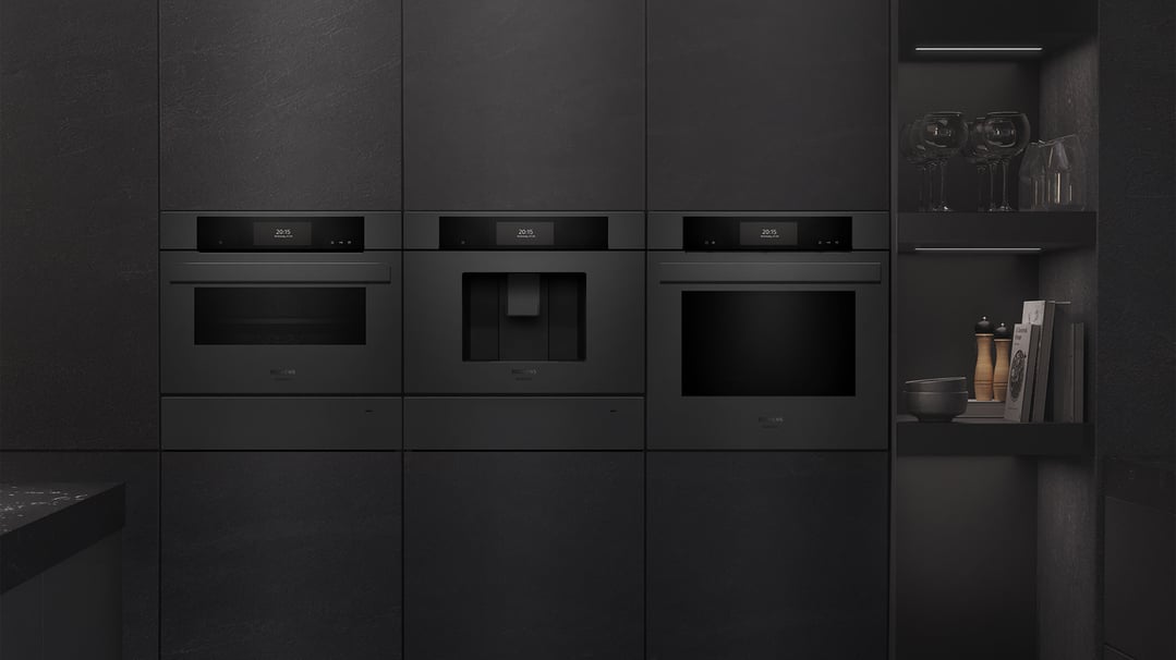 Three built-in kitchen appliances, including a coffee machine, in a dark kitchen