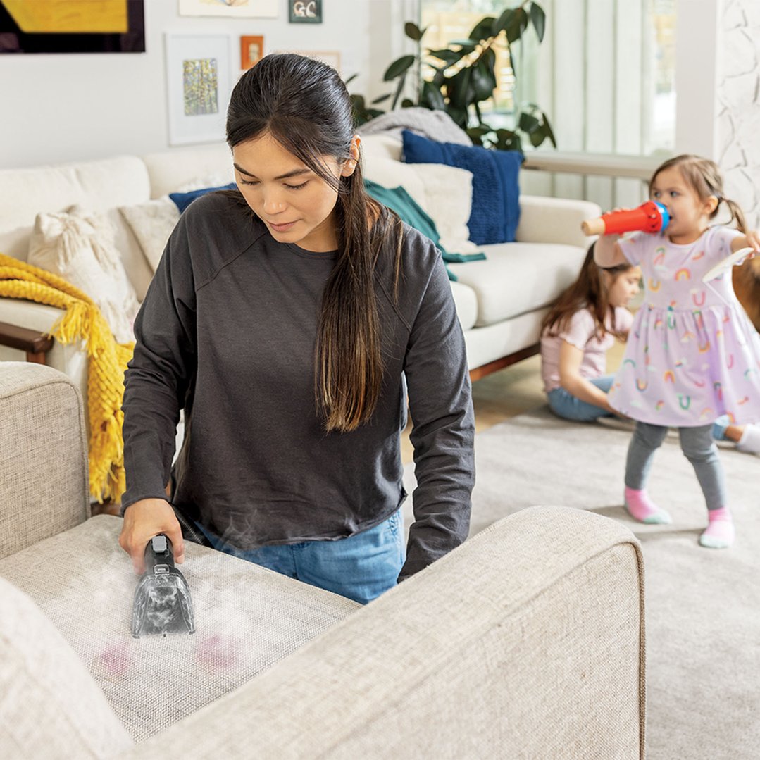 Woman using a BISSELL SpotClean HydroSteam vacuum cleaner on a sofa