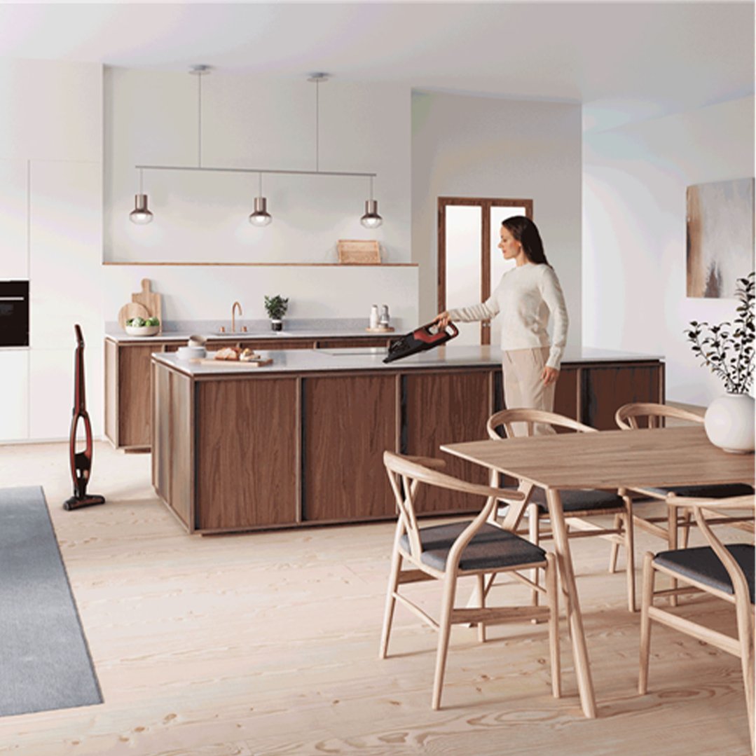 Woman using a handheld vacuum in a modern kitchen with a standing vacuum