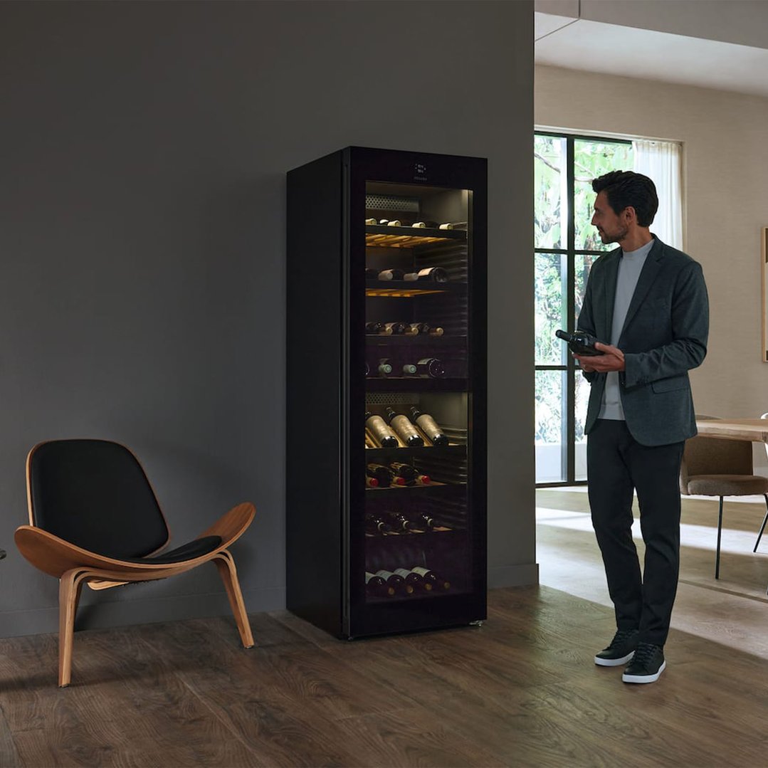 Man holding a wine bottle next to a tall wine conditioning unit