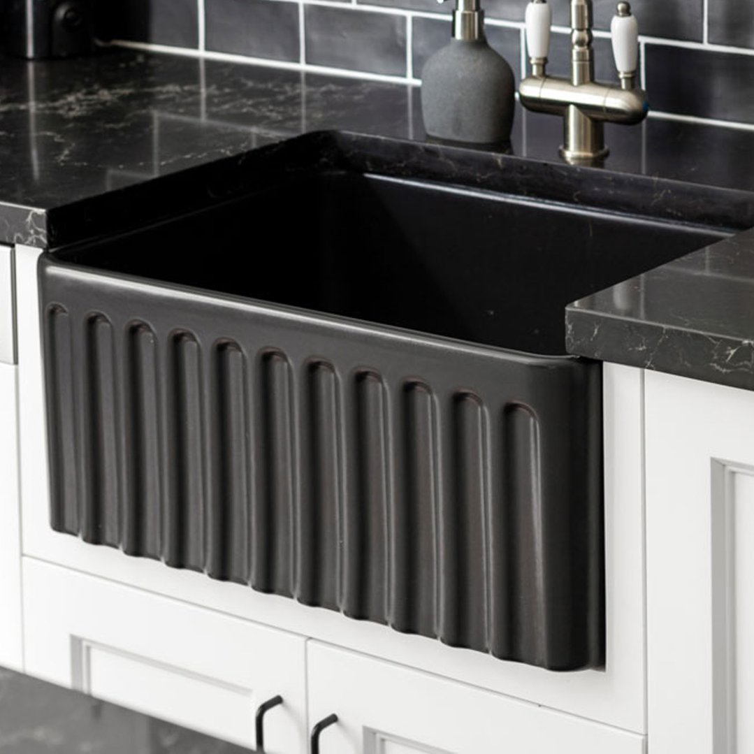 A black fireclay butler sink installed in a kitchen with black countertops