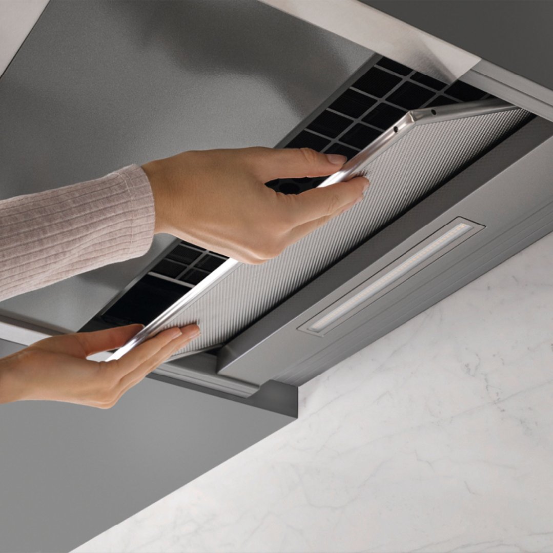 Hands removing the metal filter from a Miele rangehood in a kitchen
