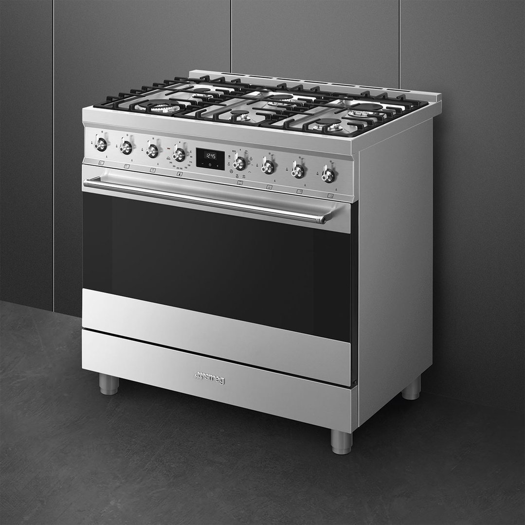Stainless steel freestanding cooker with six burners and an oven in a dark kitchen