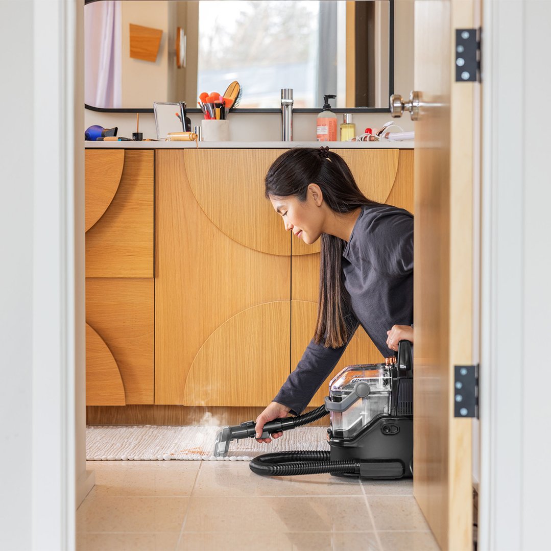 Woman using a vacuum cleaner to clean a rug in a bathroom