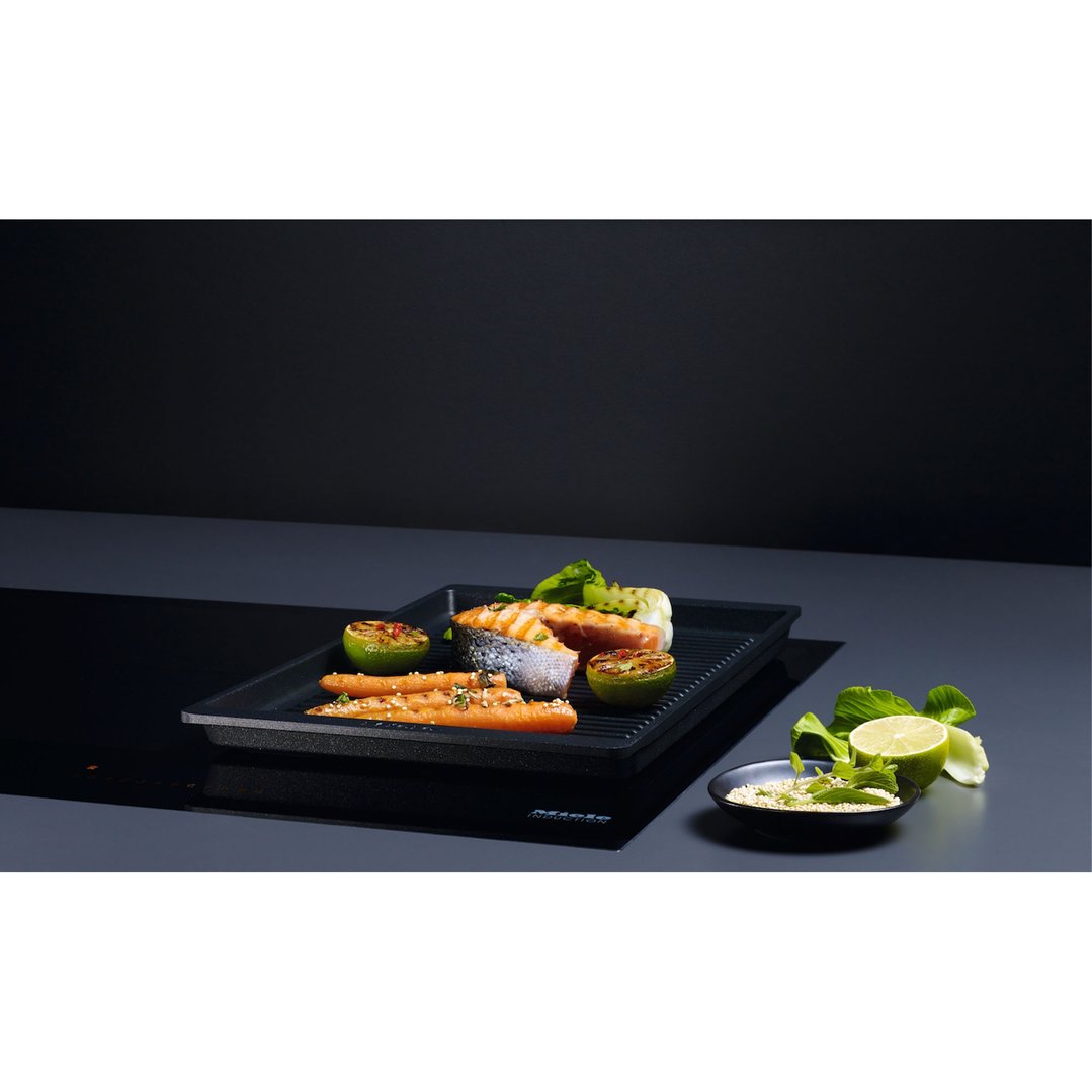 Grilled salmon, carrots, and limes on a grill pan on an induction cooktop