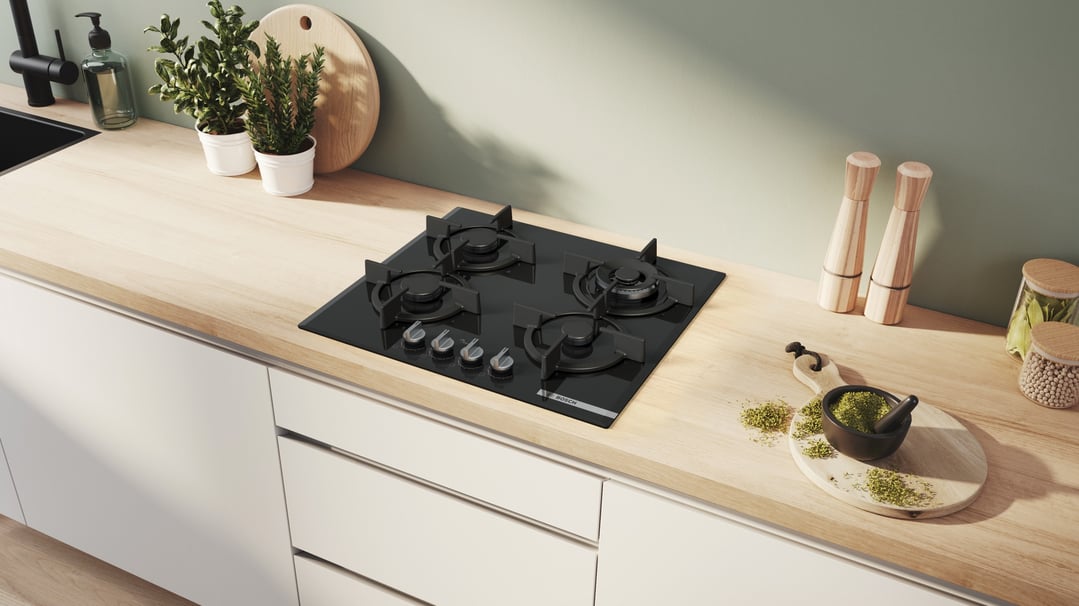 Black Bosch gas cooktop on a wooden kitchen counter with plants and spices