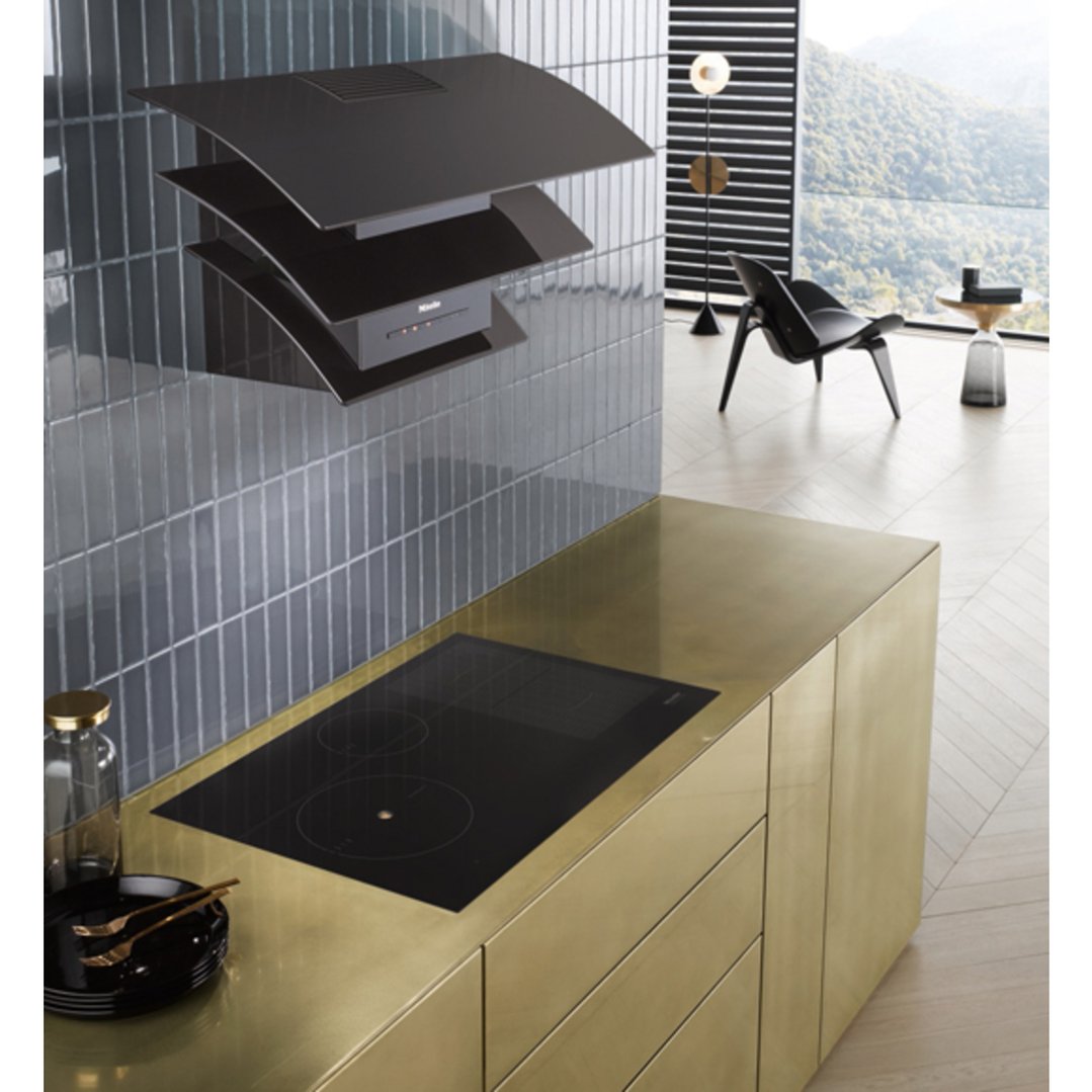 Black wall-mounted rangehood and cooktop in a modern kitchen with gold cabinetry
