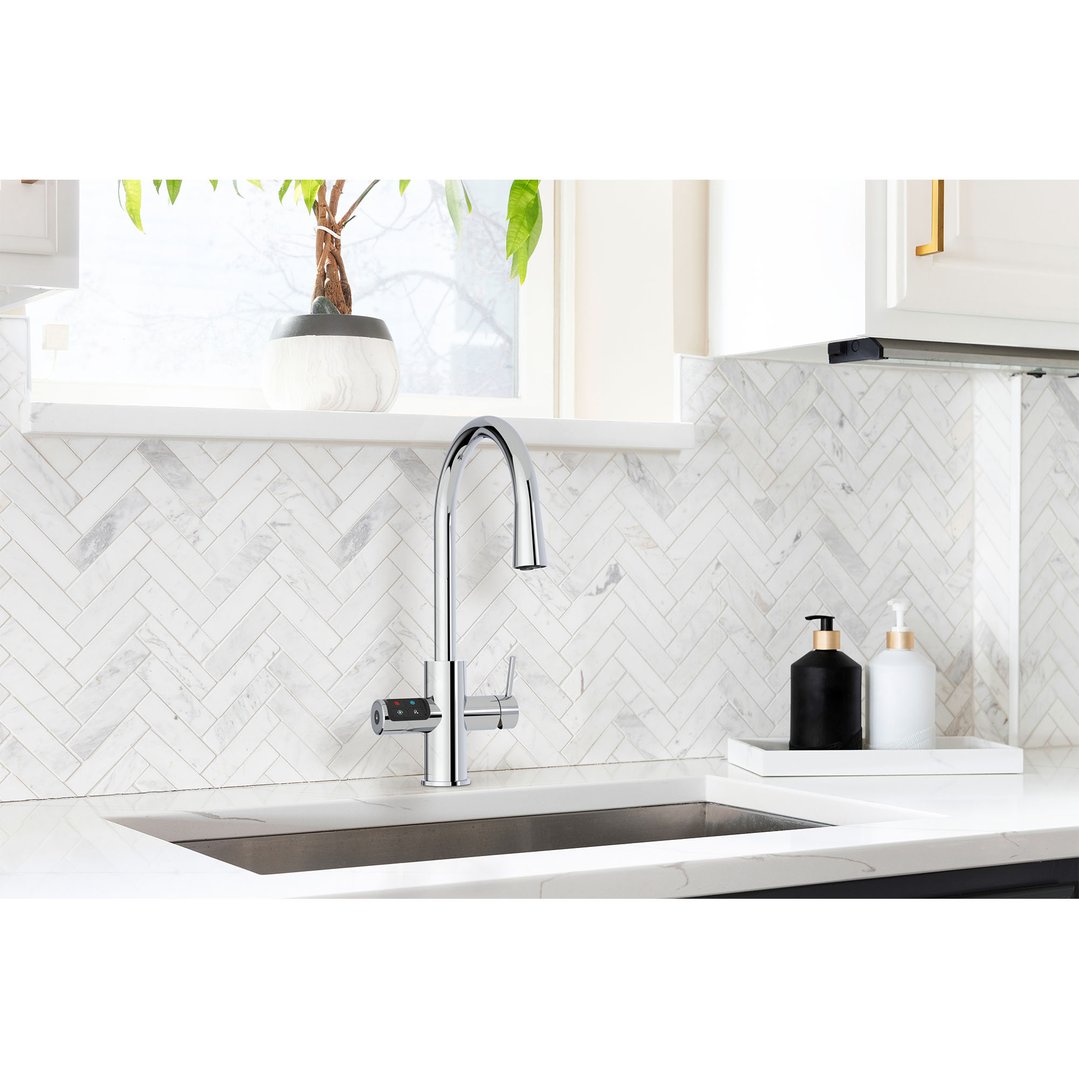 Chrome tap in a kitchen with white herringbone tile backsplash and plant