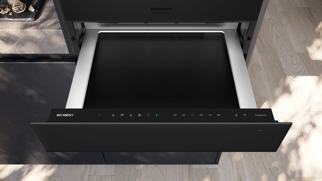 A black Siemens warming drawer with controls open in a modern kitchen setting