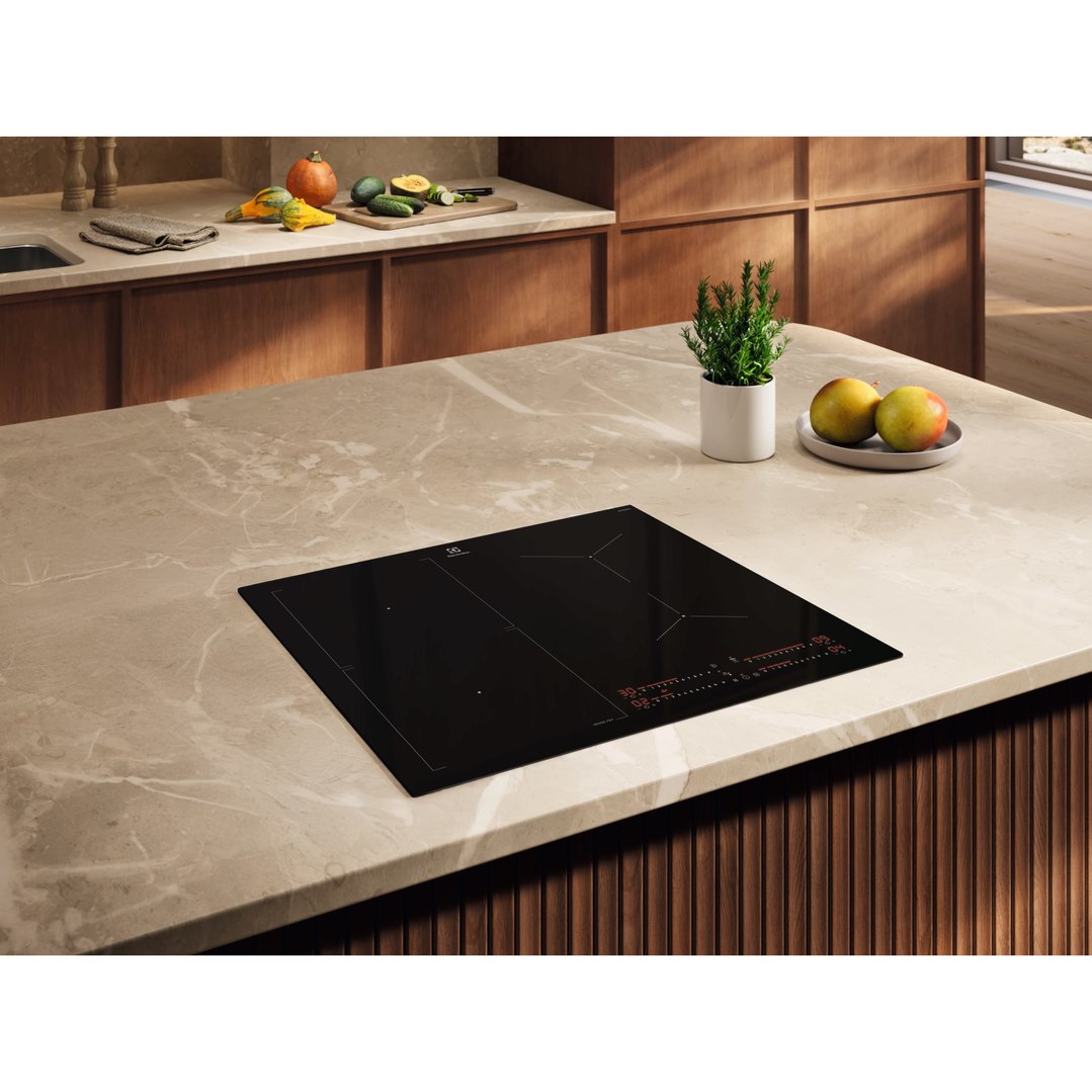 Black induction cooktop on a marble kitchen island with vegetables and fruit